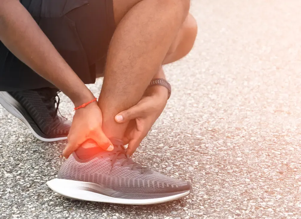 A runner crouched on a footpath holding the outside of their ankle, the joint highlighted
