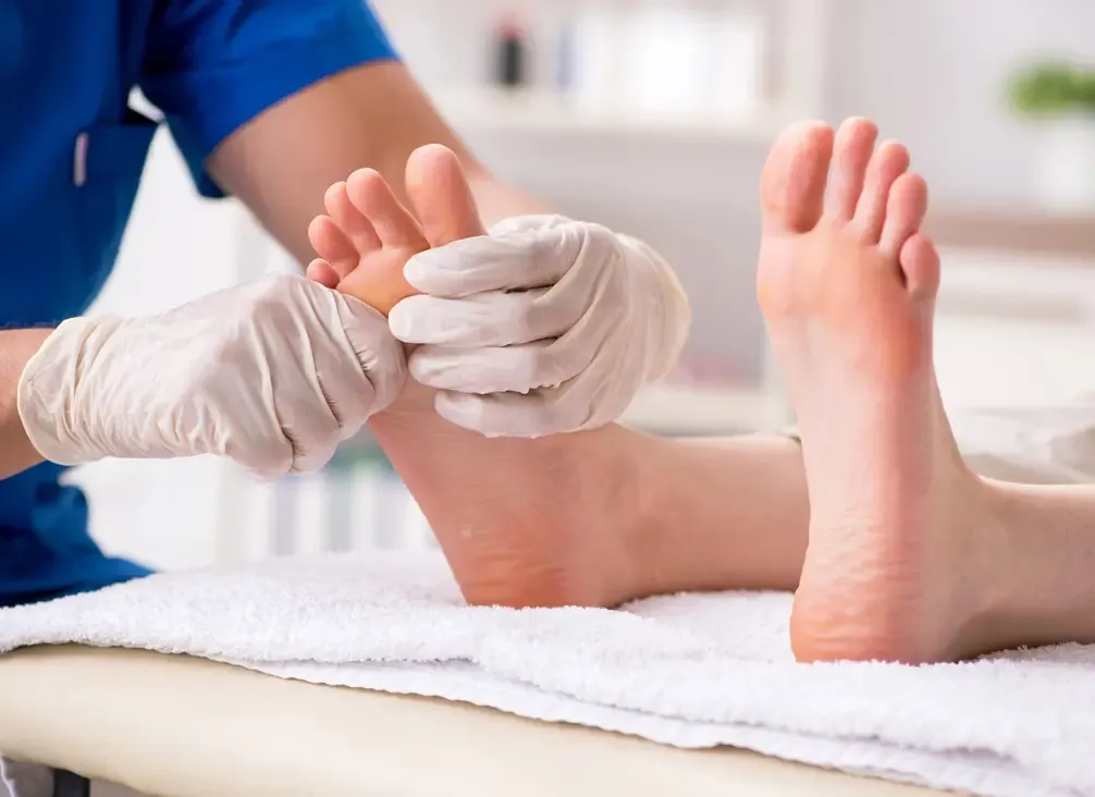A podiatrist in gloves examining the toes of a bare foot on a treatment couch