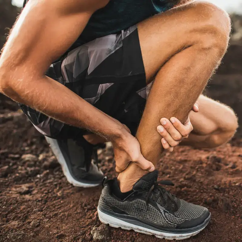 Man holding Achilles tendon after running on uneven terrain