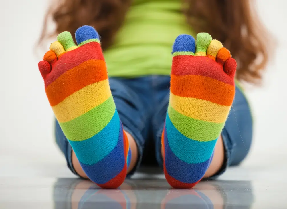 Child wearing colourful rainbow toe socks sitting on floor, showing healthy foot posture.