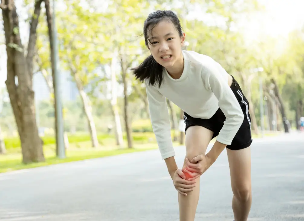Teen girl holding painful knee during outdoor run – possible Osgood-Schlatter disease