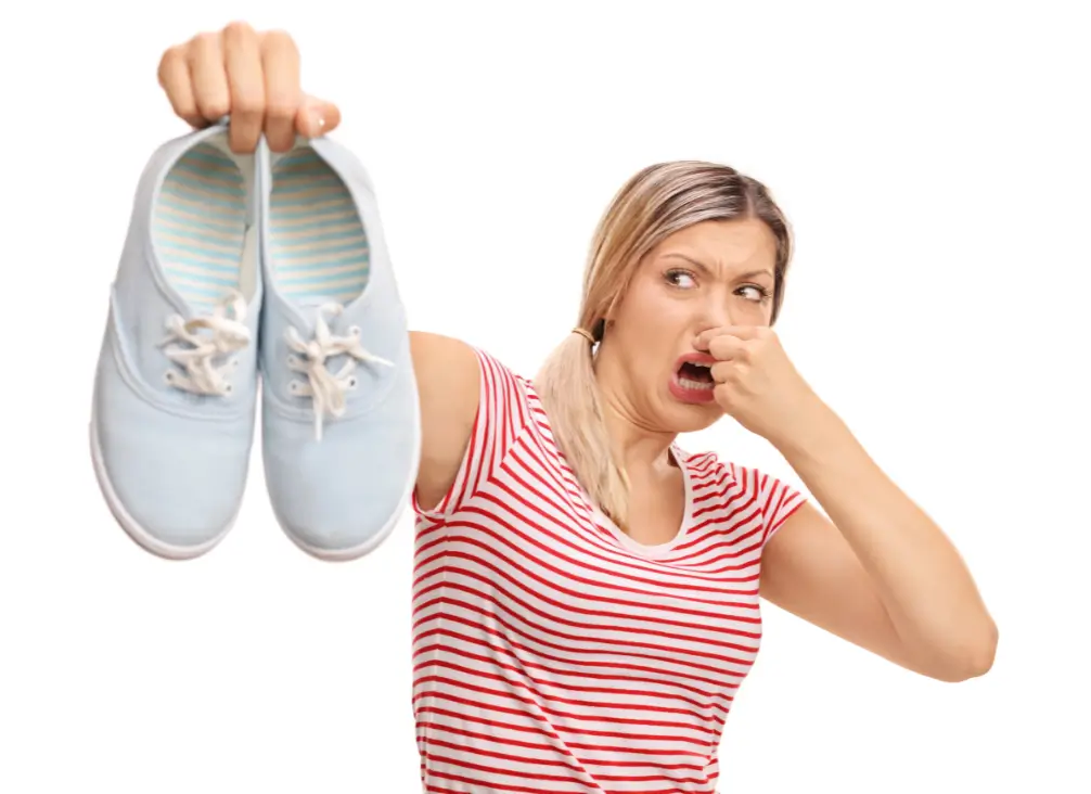 Woman holding smelly shoes and pinching nose in disgust